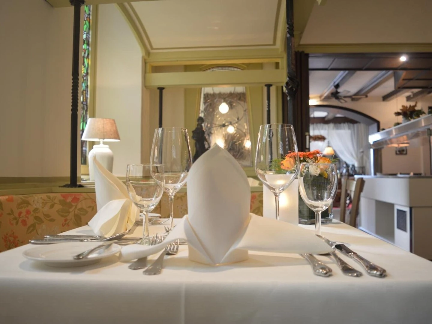 Gedeckter Tisch mit weißer Tischdecke, gefalteten Servietten, Weingläsern, Besteck und einer kleinen Blumendekoration in einem Restaurant