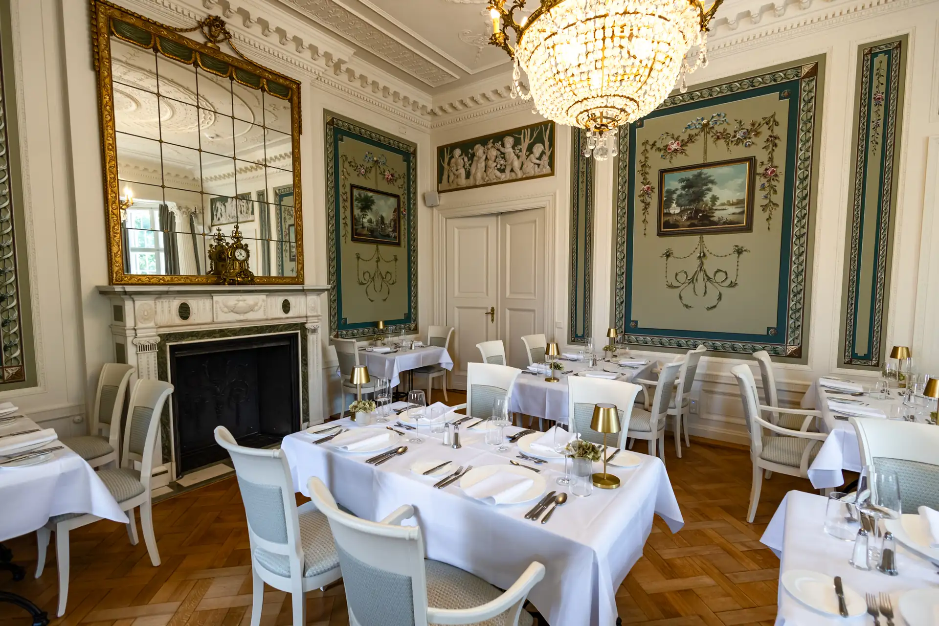 Elegantes Restaurant im Schlosshotel Neustrelitz mit weißen Tischdecken, goldenen Lampen, Stühlen mit weißen Polstern, großem Spiegel über einem Kamin und klassischer Wanddekoration
