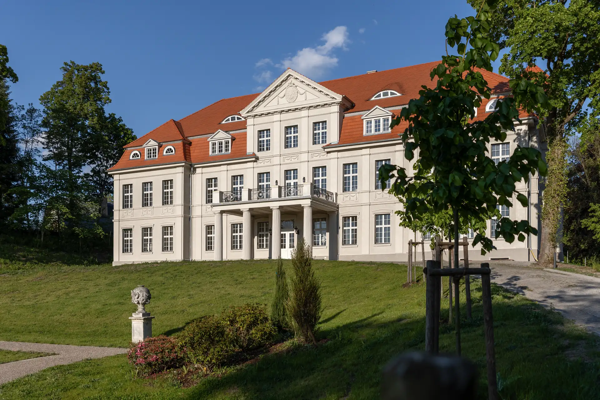 Schlosshotel Neustrelitz mit klassizistischer Fassade, dreigeschossig, rotem Satteldach und Säulenportikus, umgeben von Rasen und Bäumen