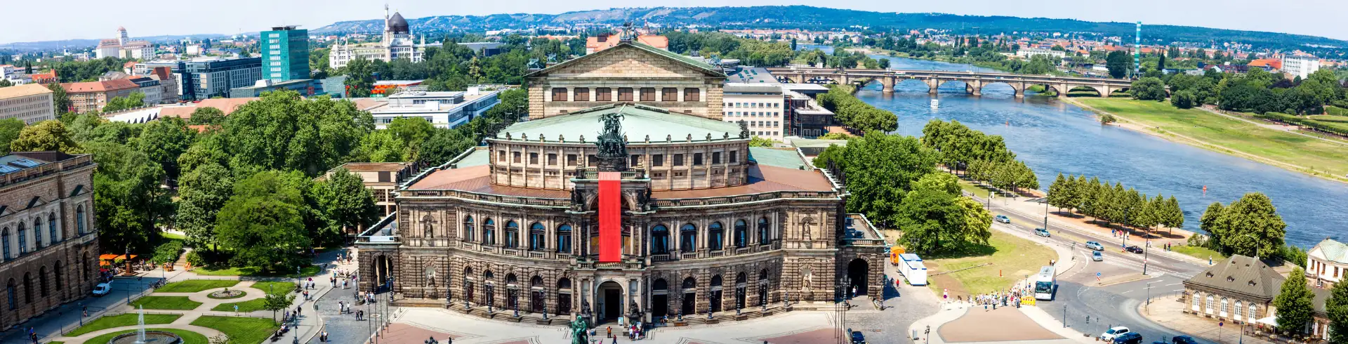 Semperoper Dresden im Bannerformat: Blick von schräg oben auf die Semperoper und den Vorplatz im Sommer mit der Elbe im Hintergrund.