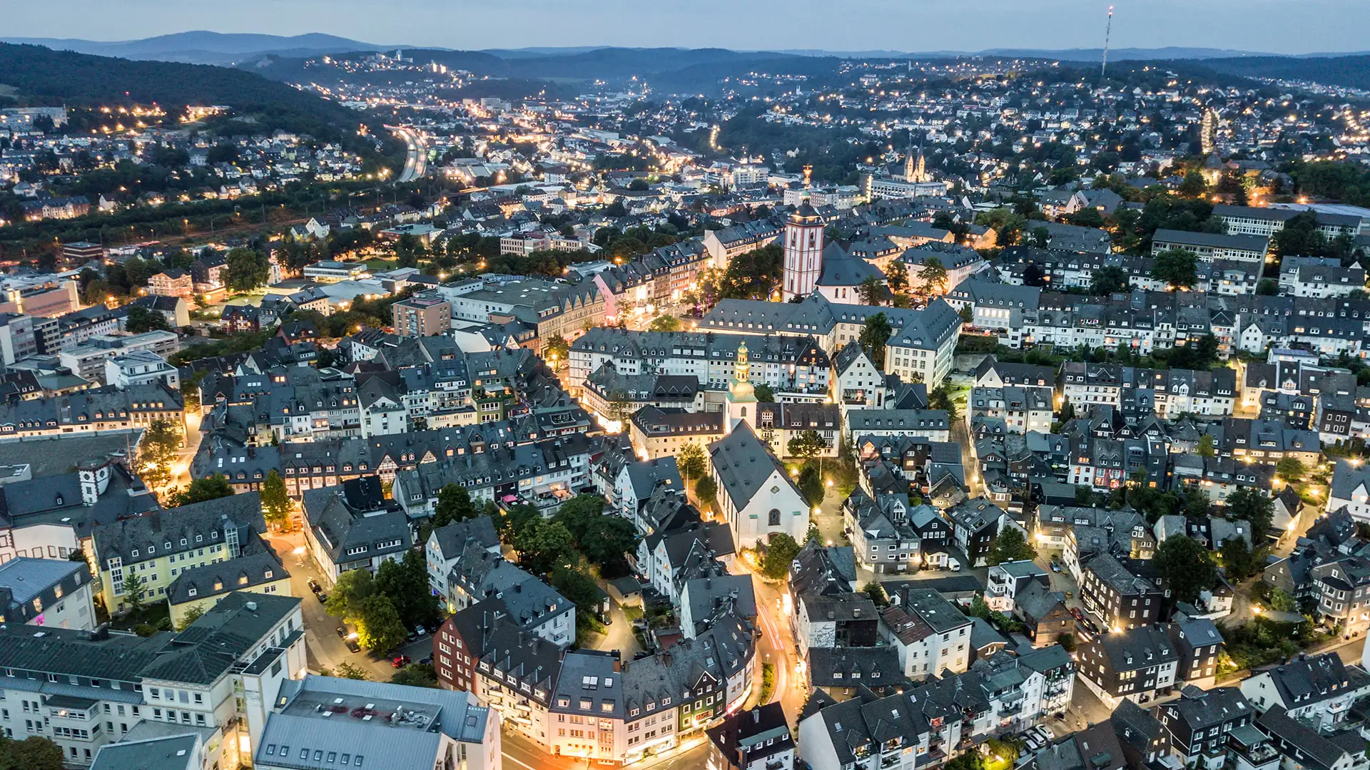 Luftaufnahme der Stadt Siegen bei Dämmerung mit beleuchteten Straßen und historischen Gebäuden (1920x1080px)