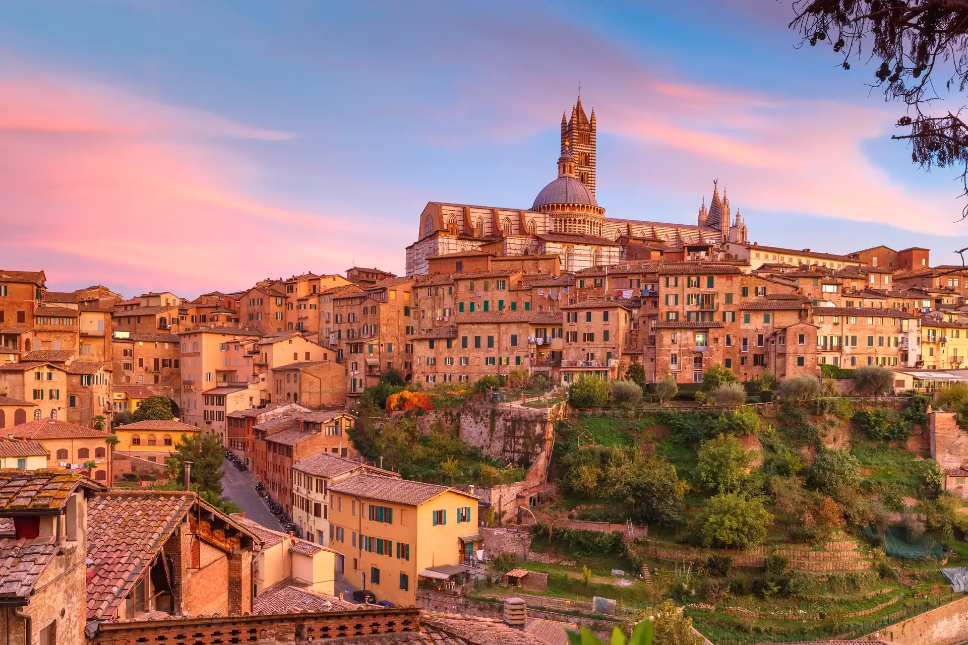 Historische Stadt Siena mit dicht aneinandergebauten Häusern und der markanten Kathedrale auf einem Hügel bei Sonnenuntergang.