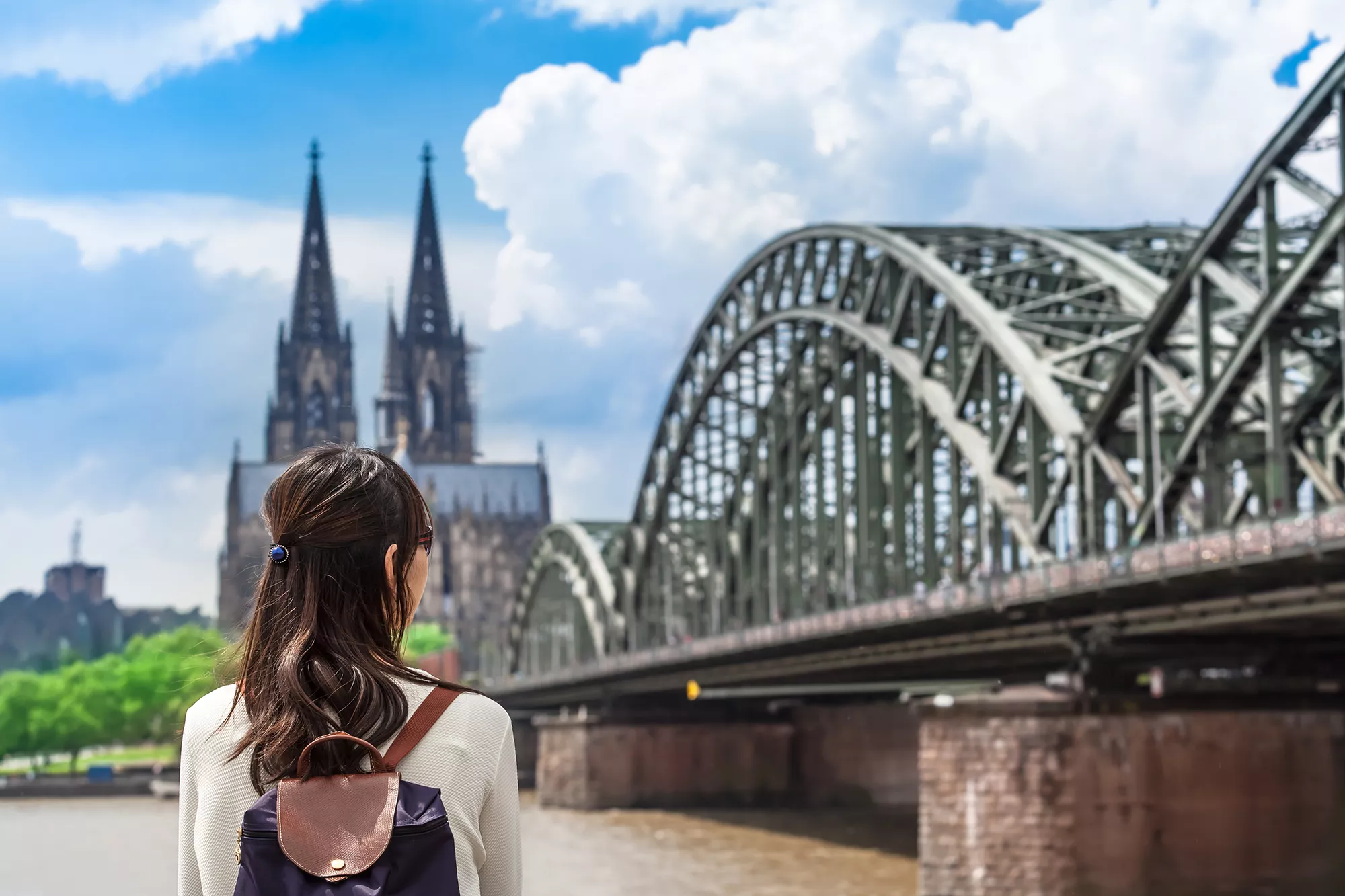 Touristin steht am Rhein und blickt auf die Hohenzollernbrücke und den Dom der Stadt Köln