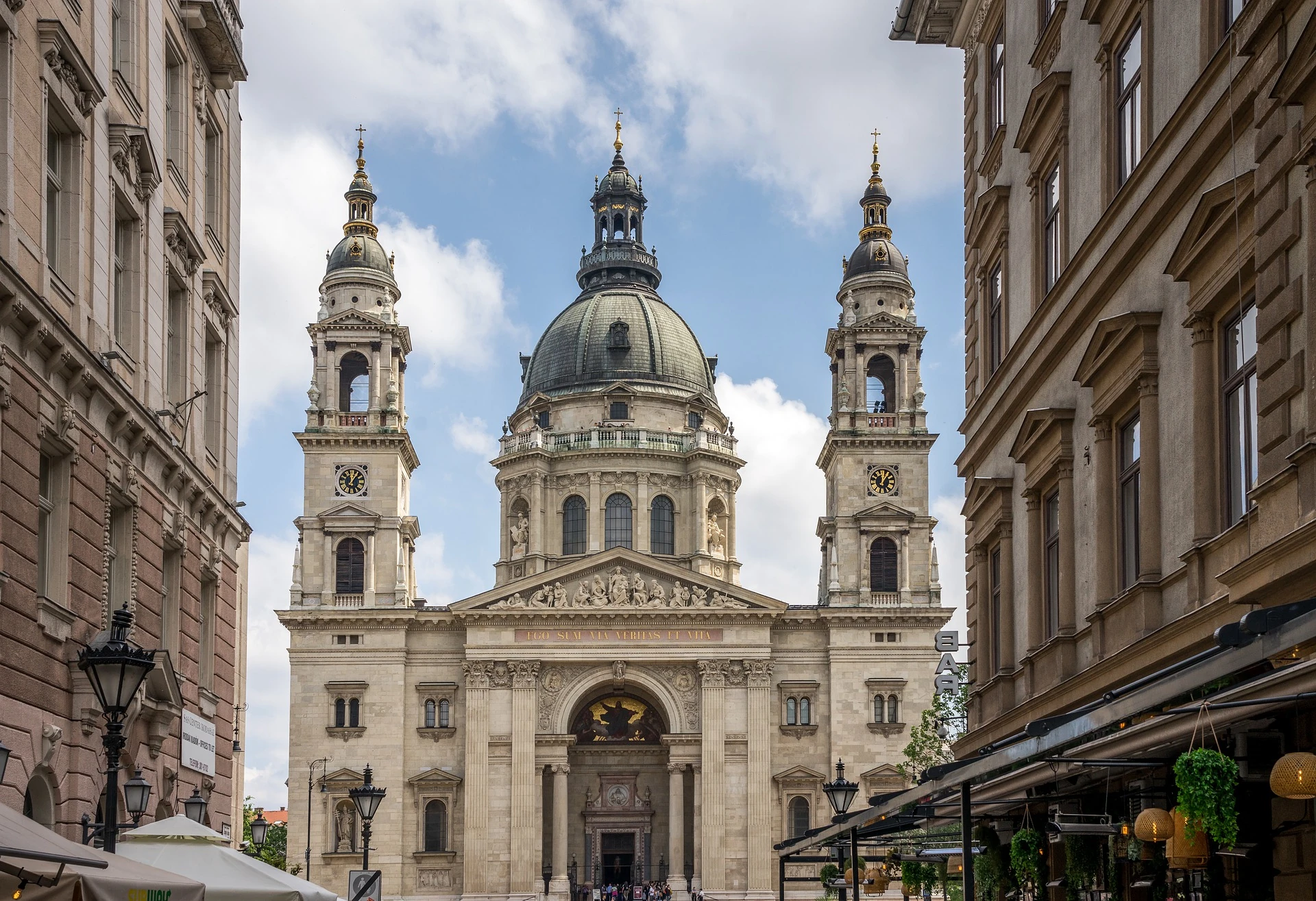 Städtereise Budapest zeigt die prächtige Fassade der St.-Stephans-Basilika, umgeben von historischen Gebäuden, mit ihren markanten Türmen und Kuppeln unter einem wolkigen Himmel.