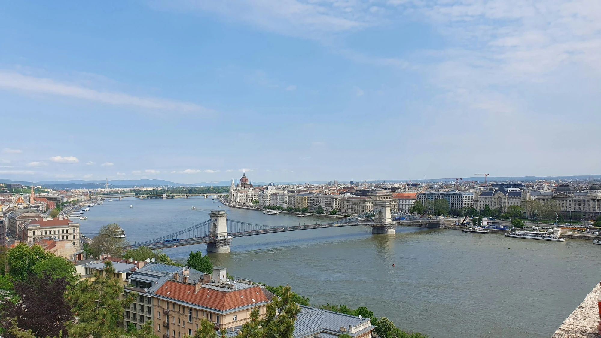 Städtereise Budapest zeigt einen Panoramablick auf die Donau mit der Kettenbrücke und dem ungarischen Parlamentsgebäude im Hintergrund unter einem klaren, blauen Himmel.
