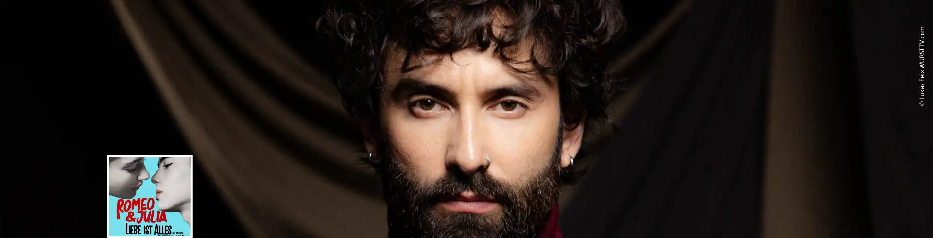 Porträt von Tom Neuwirth / Conchita Wurst mit lockigem Haar vor schwarzem Hintergrund, trägt ein schwarzes Oberteil. Ergänzt mit kleinem Logo vom Romeo & Julia Musical in Berlin, links unten.