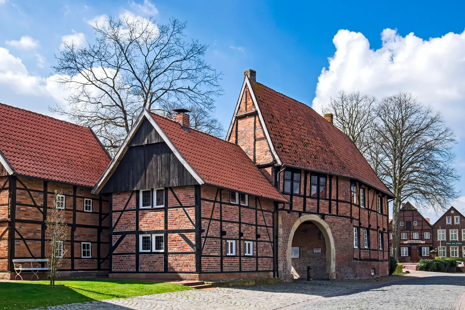 Fachwerkgebäude mit rotem Ziegeldach und großem Torbogen unter blauem Himmel an der Hunnenpforte des Stifts Asbeck
