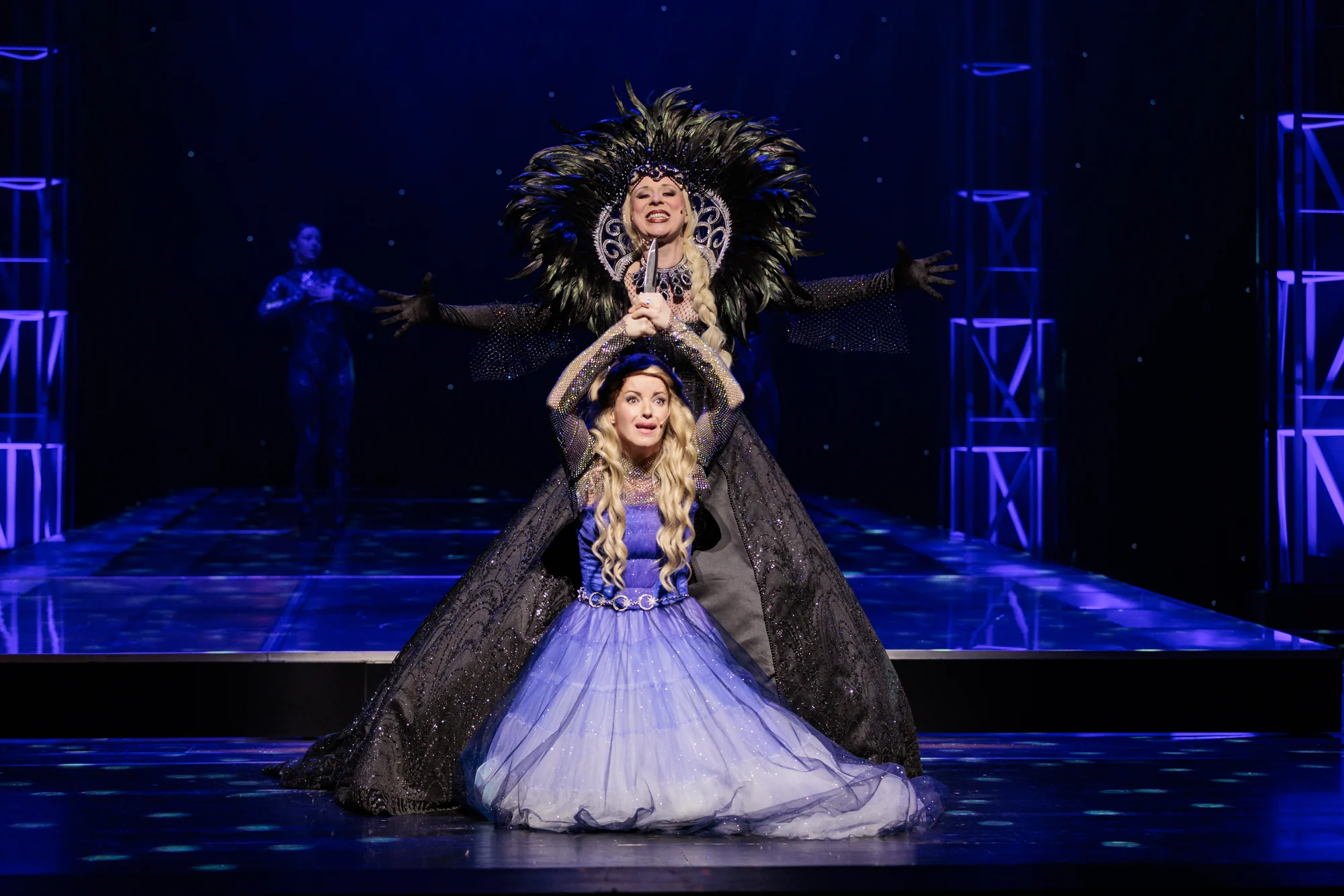 Die Königin der Nacht in schwarzen Kostüm steht hinter ihrer Tochter Pamina und will ihr den für Sarastro bestimmten Morddolch geben