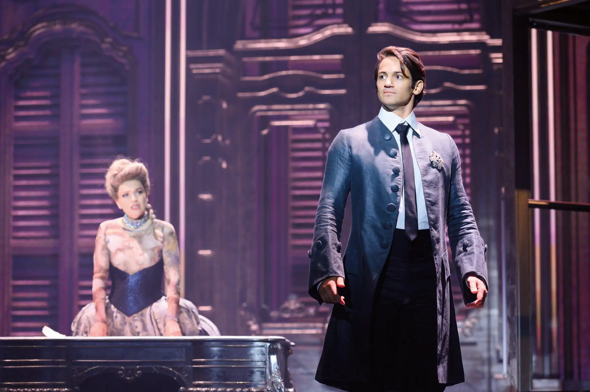 Maria Theresia Musical Szenenfoto: Mann in blauem Frack und Krawatte steht vor einer Frau in barockem Kleid mit Korsett, beide auf Bühne mit prunkvollem Hintergrund.