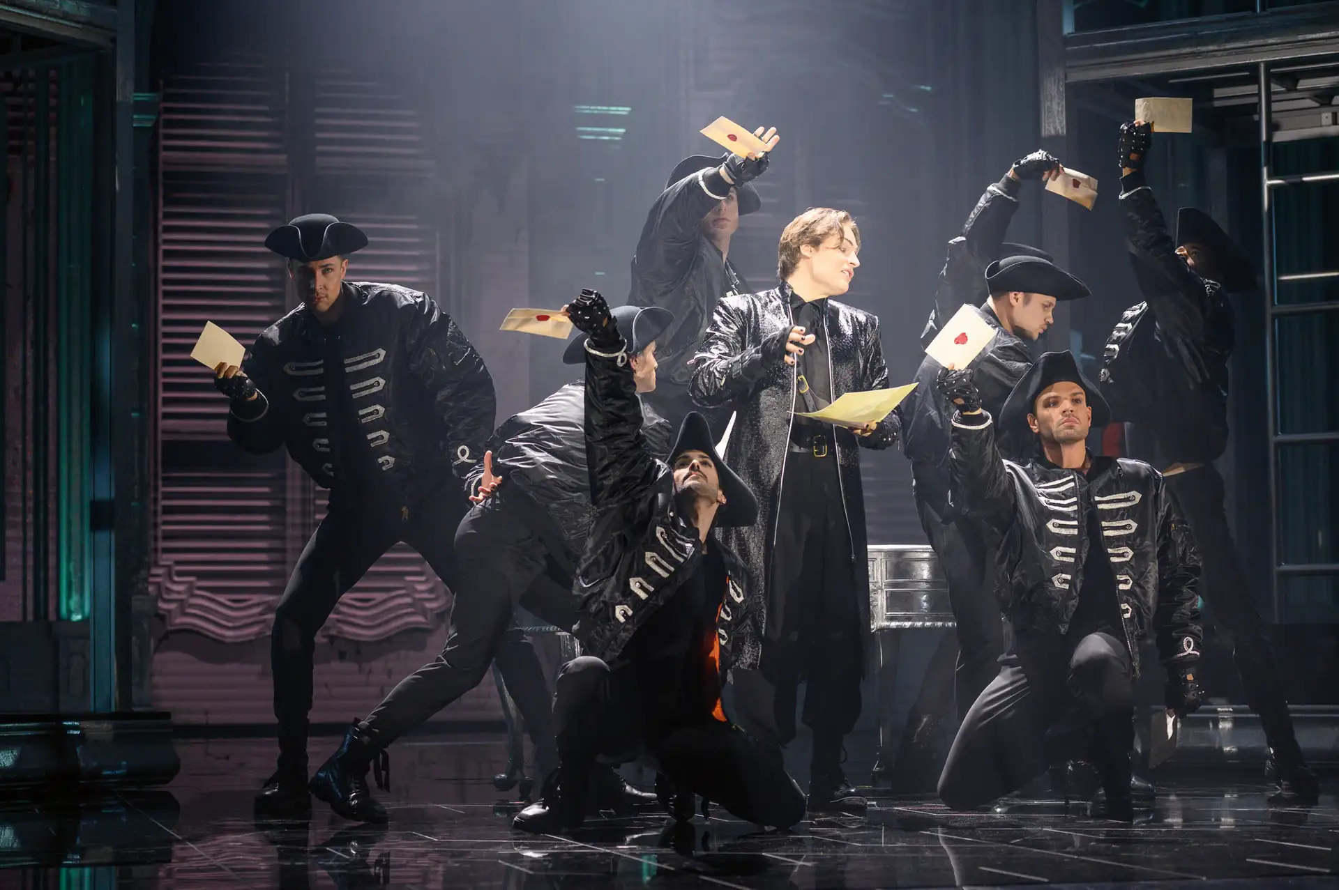 Maria Theresia Musical Szenenfoto: Mehrere Personen in schwarzen Kostümen mit silbernen Verzierungen halten Briefe in die Luft, Bühnenbeleuchtung und dunkler Hintergrund.