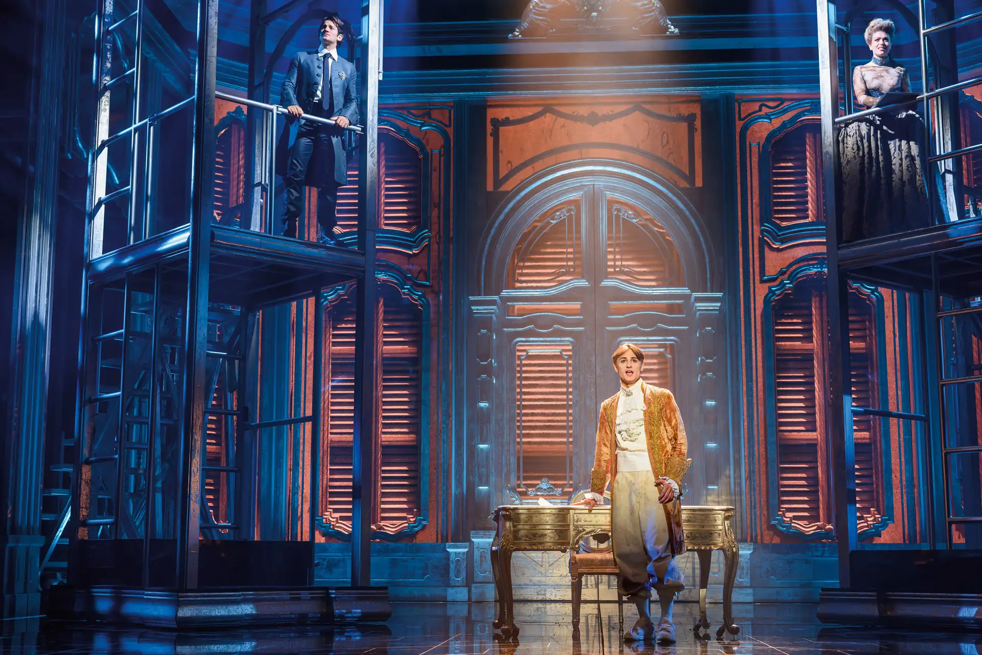 Maria Theresia Musical Szenenfoto: Bühnenbild mit zwei Personen in historischer Kleidung, eine steht auf einer erhöhten Plattform, die andere vor einem antiken Schreibtisch mit Stuhl.