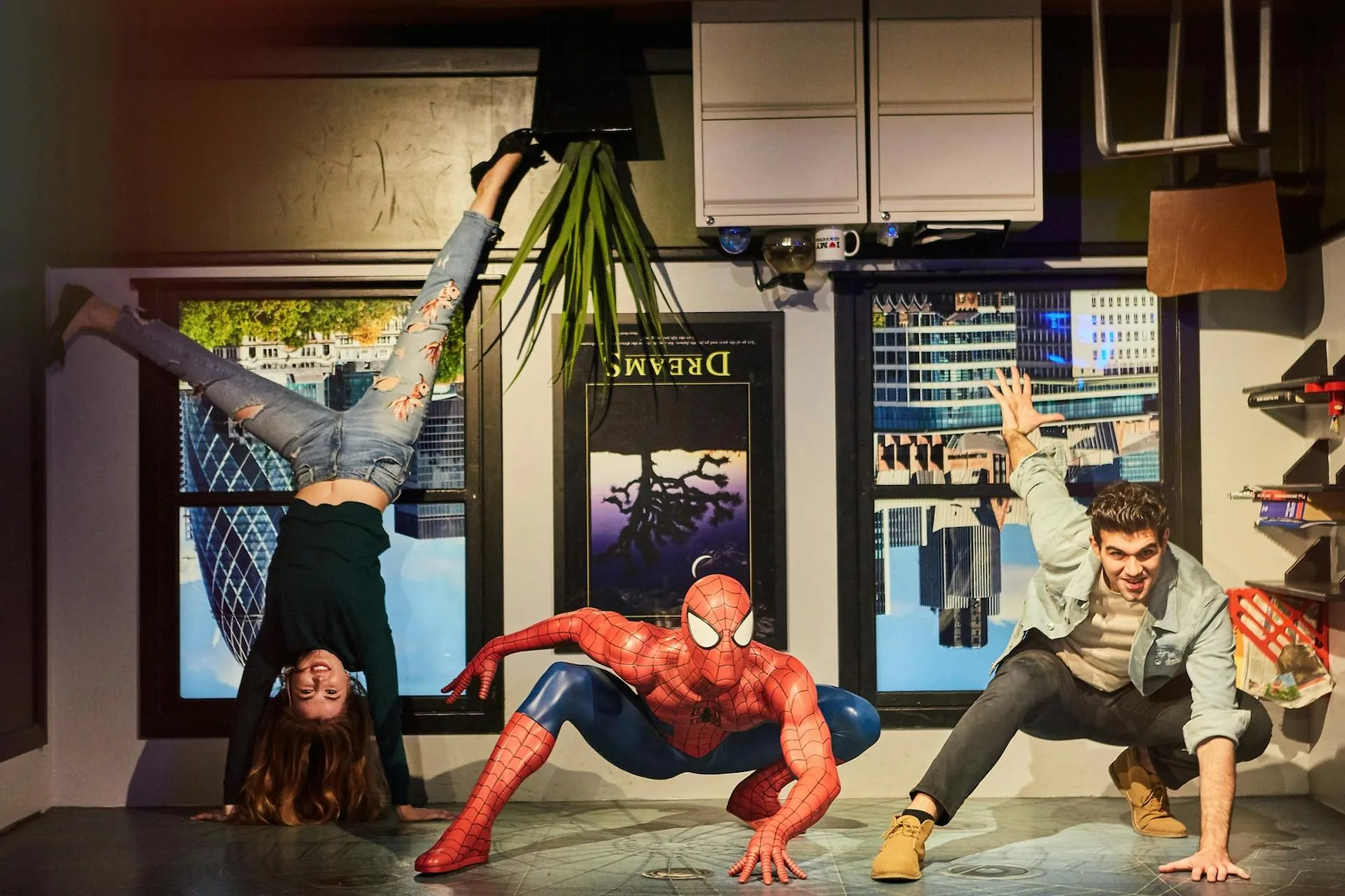Madame Tussauds London - Raum auf den Kopf gestellt, Spiderman hängt auf dem Boden, Jugendlicher posiert neben Spider-Man, Frau macht Handstand