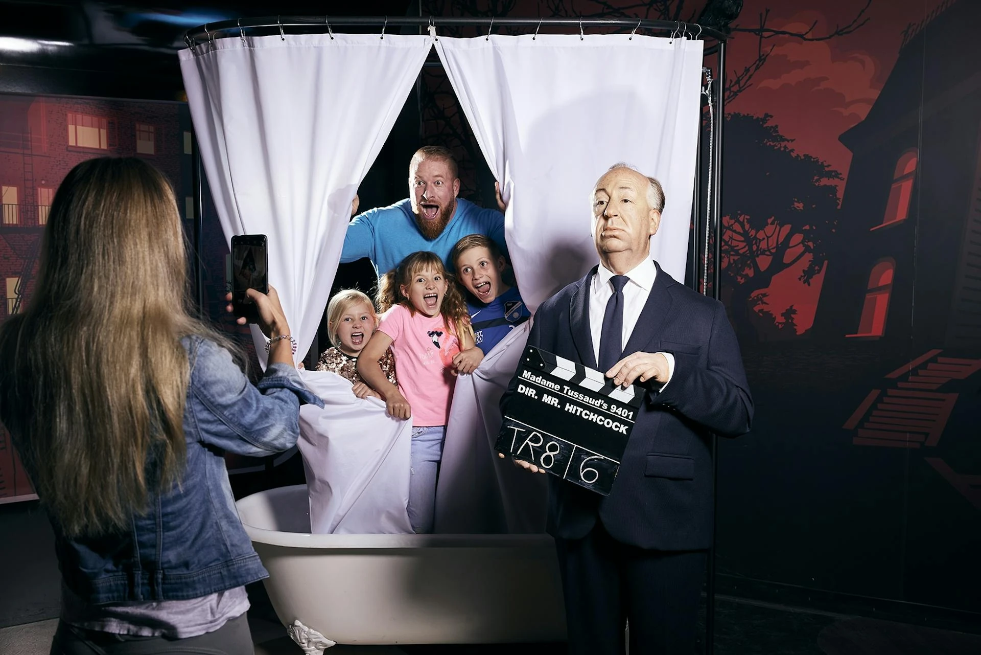 Madame Tussauds Wien - Vater und Kinder posieren schreiend aus einem Badewannen-Vorhang während Regisseur Alfred Hitchcock davor steht, Frau macht Foto