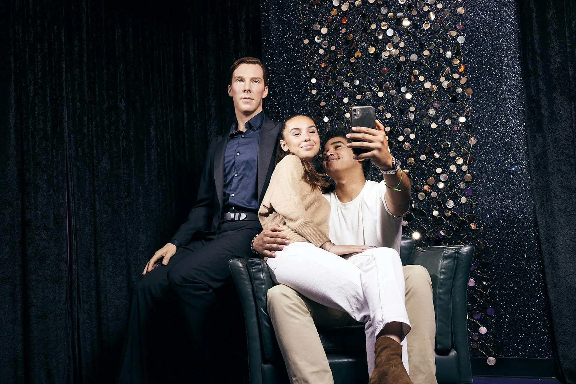 Madame Tussauds Wien - junges Päärchen auf einem Sessel machen Selfie, während Falco hinter den beiden sitzt