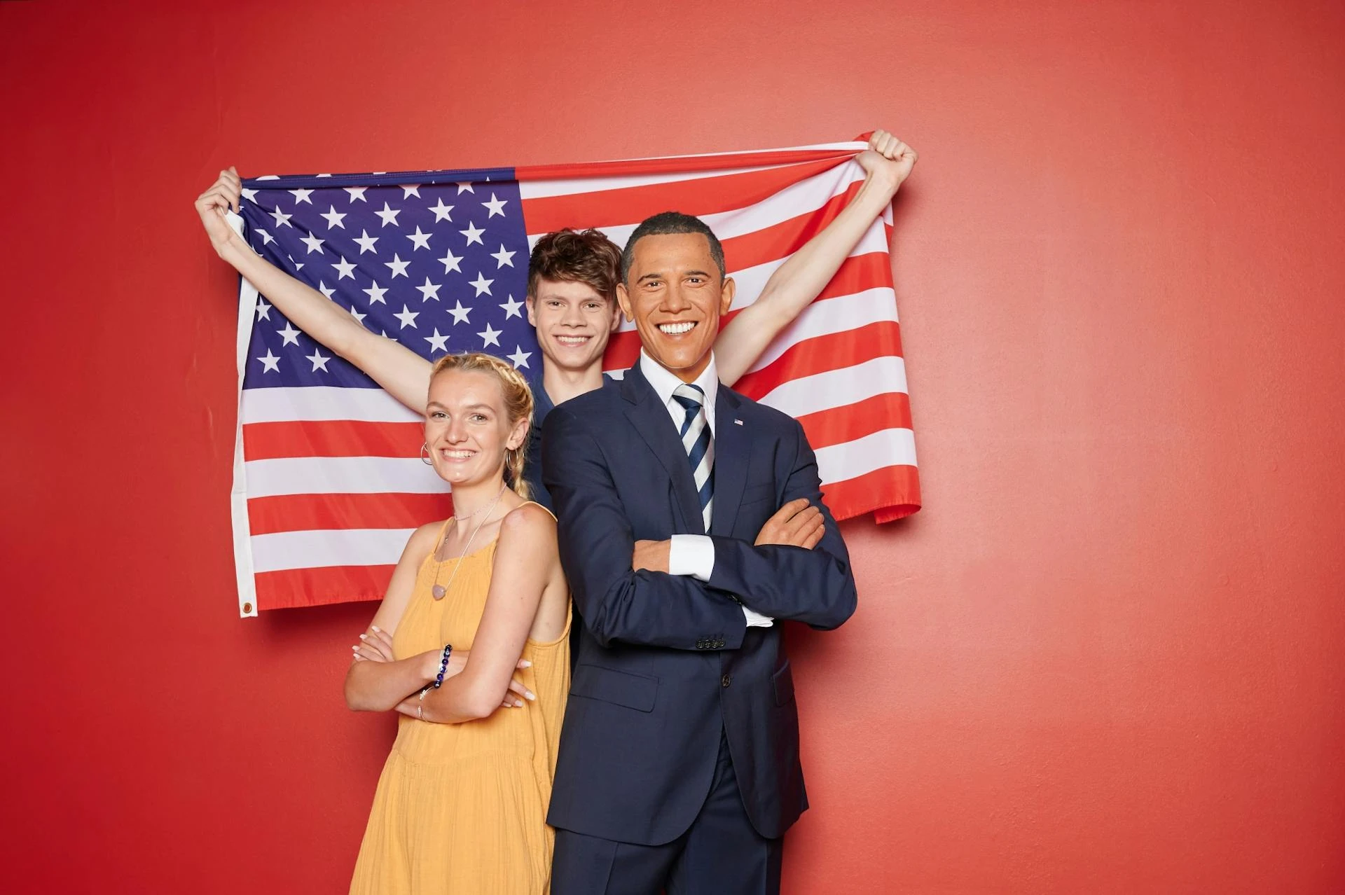 Madame Tussauds Berlin - Barack Obama im roten Hintergrund, Besucher posieren neben ihm und halten USA Flagge hoch