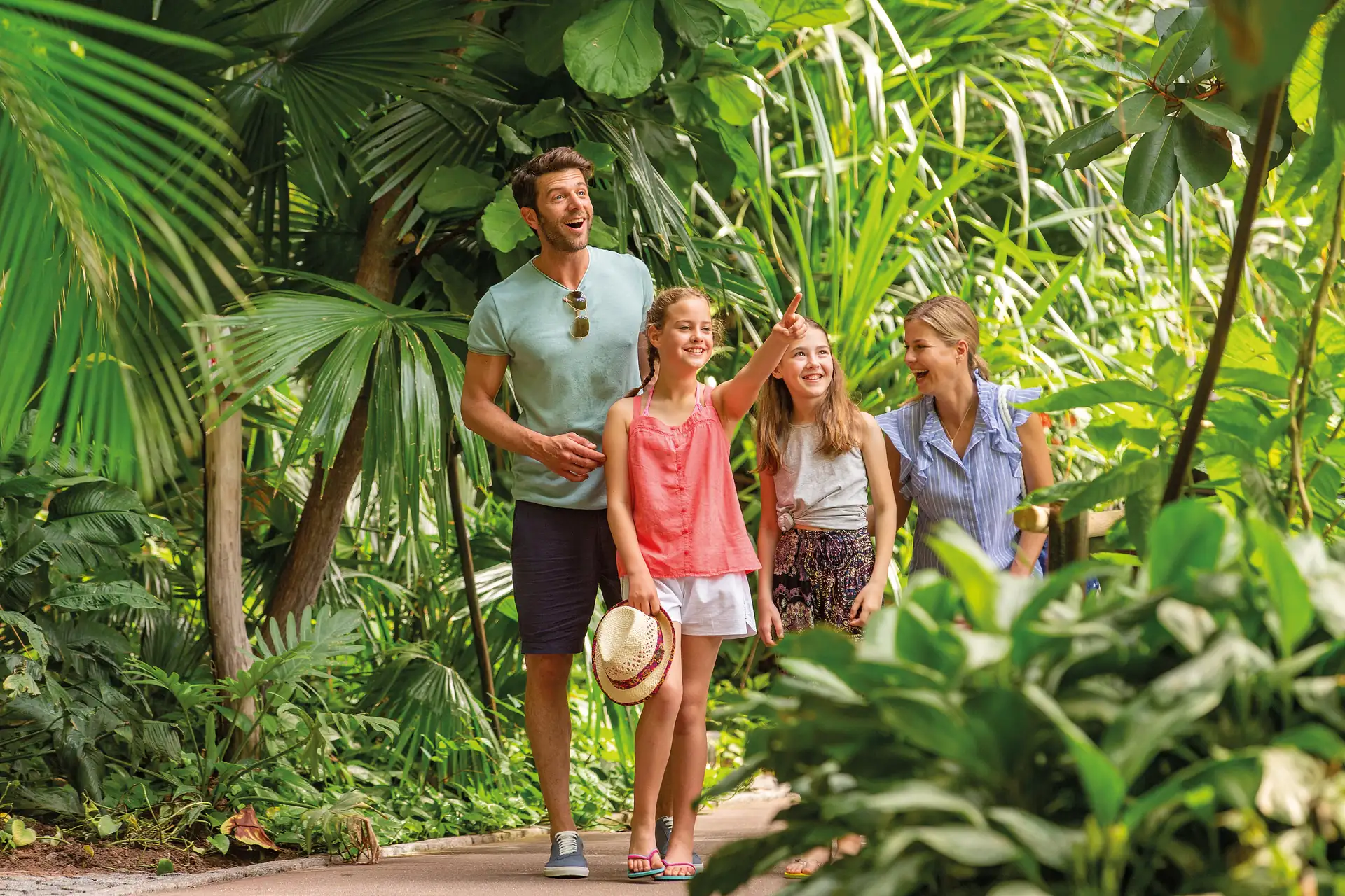 Familie im Regelwald des Tropical Islands: Familie mit Vater, Mutter und zwei Kindern auf einem Weg im tropischen Regenwald, umgeben von üppigem Grün.
