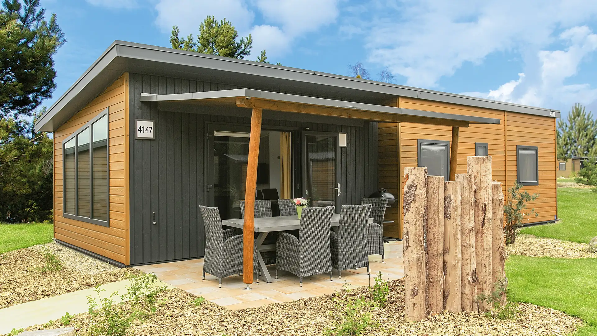 Modernes Sunrise Homes Ferienhaus mit Holzverkleidung und überdachter Terrasse mit Gartenmöbeln auf Rasenfläche