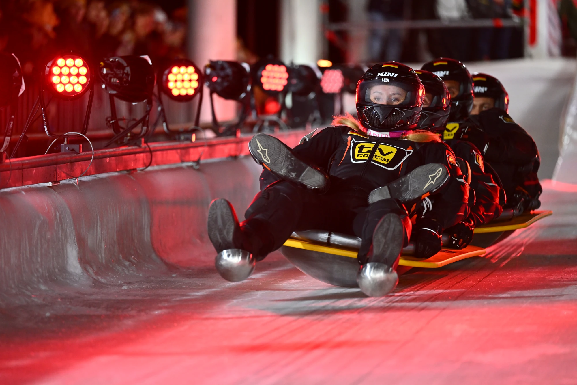 Team beim Bobfahren mit roten Lichtern im Hintergrund.