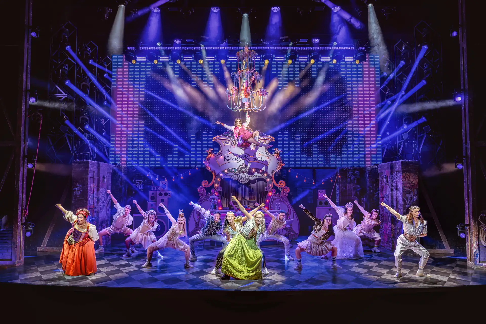 Bühnenbild des Musicals Julia in Stuttgart mit einer Gruppe von Darstellern in historischen Kostümen vor einer großen, beleuchteten Kulisse und einem Kronleuchter über der Bühne