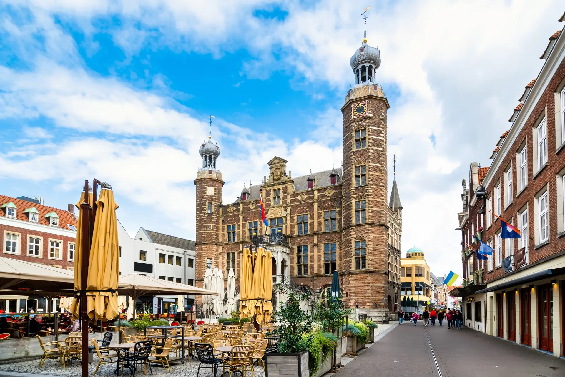 Historisches Rathaus mit zwei Türmen an einem belebten Platz mit Außengastronomie und Passanten in Venlo
