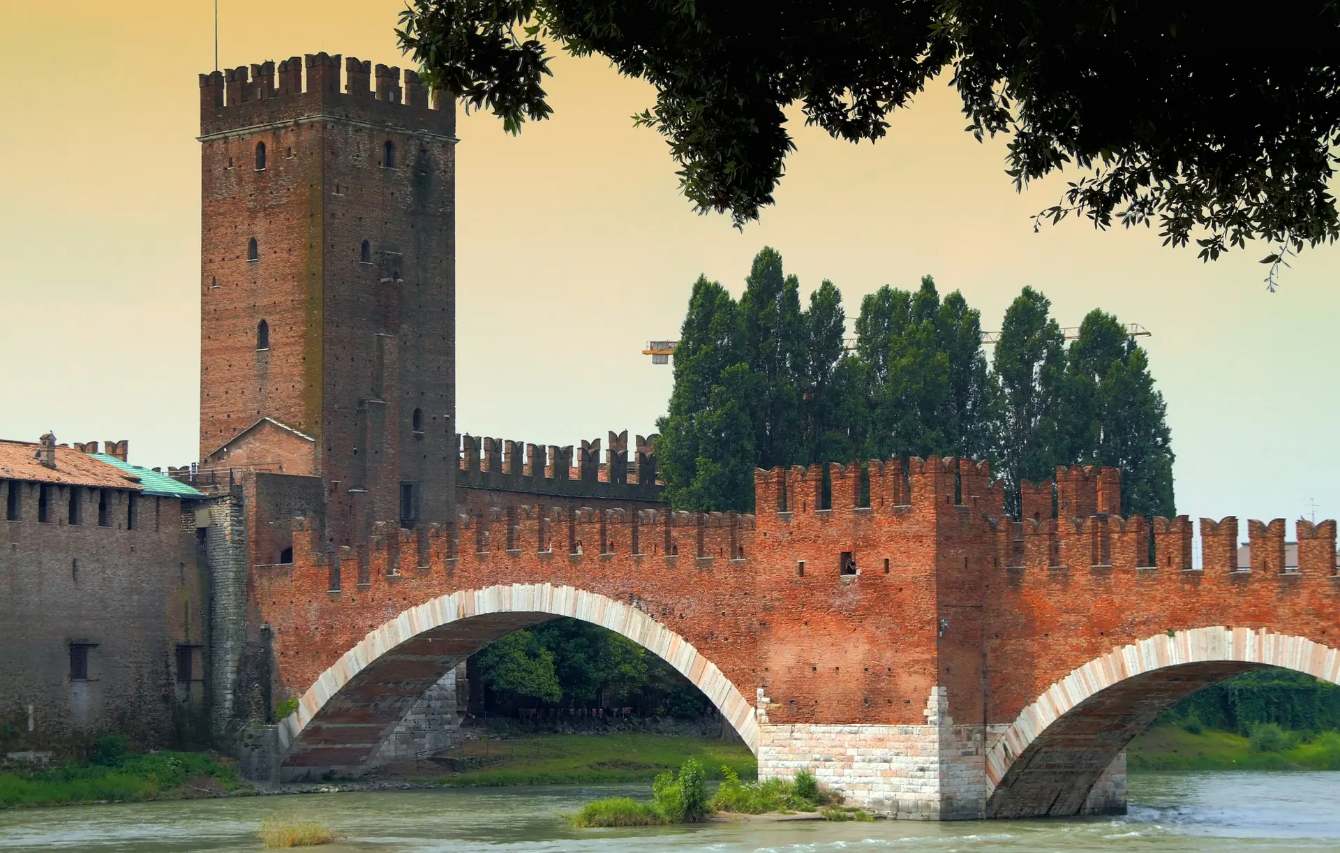 Nahaufnahme der Castelvecchio und der Ponte Scaligero, die majestätisch über die grünschimmernde Etsch führen. Die beeindruckende Architektur der Brücken spiegelt sich im ruhigen Wasser wider.