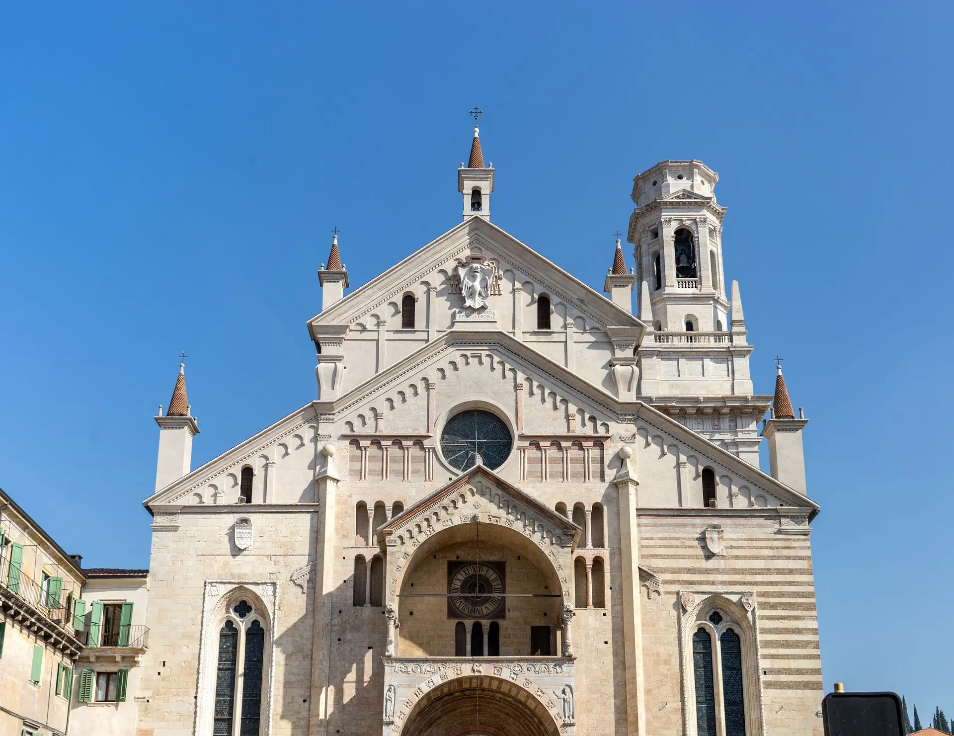 Nahaufnahme des oberen Teils des Doms von Verona, der sich majestätisch gegen den strahlend blauen Himmel abhebt. Die detailreiche Architektur und der kunstvolle Turm sind klar erkennbar und verleihen dem Bild eine beeindruckende Präsenz.