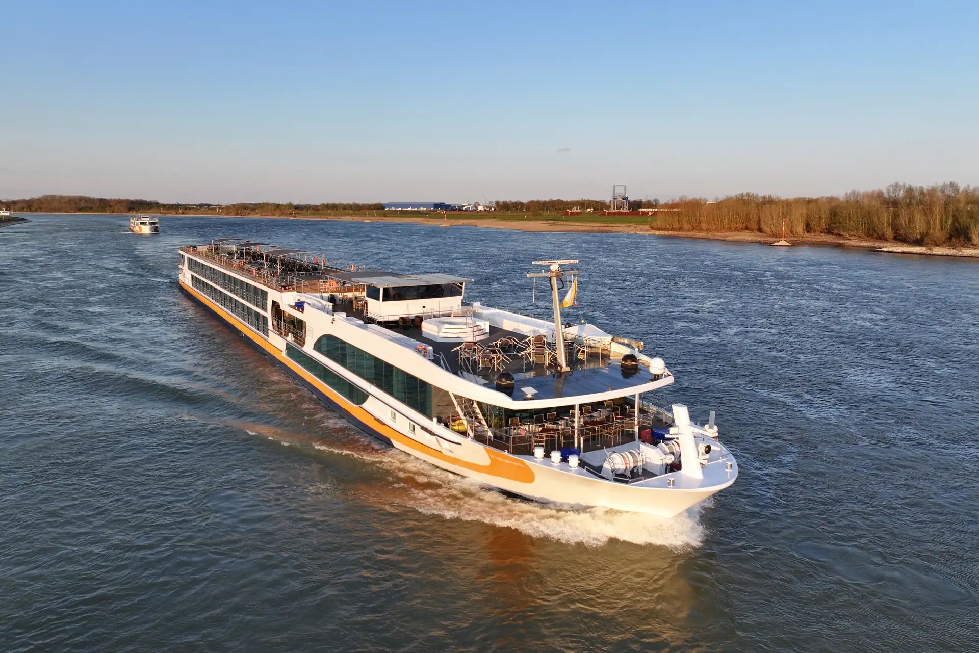 Flusskreuzfahrtschiff VistaNeo mit mehreren Decks fährt auf einem breiten Fluss, Ufer mit herbstlichen Bäumen im Hintergrund.