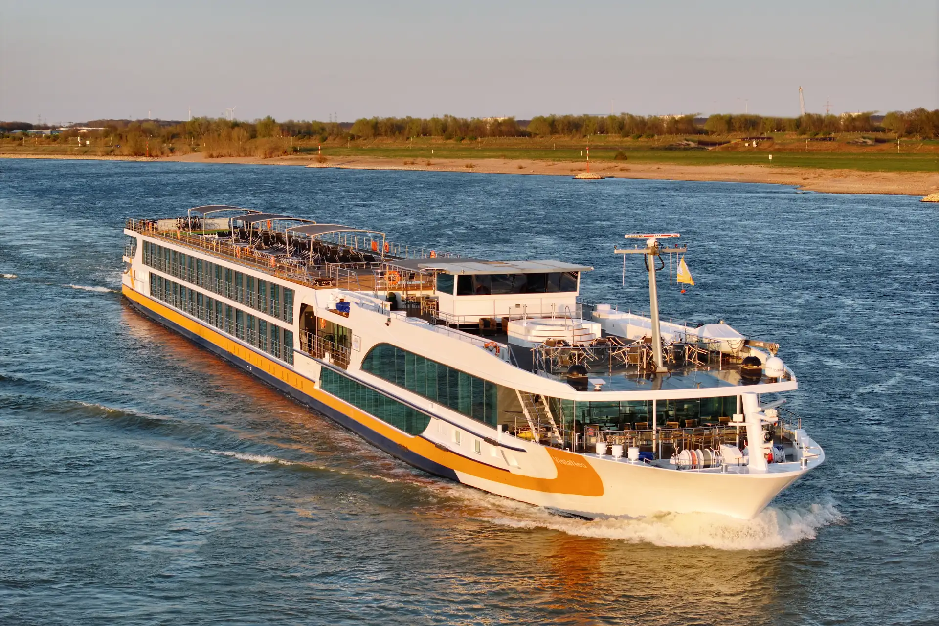 Flusskreuzfahrtschiff VistaNeo mit mehreren Decks fährt auf einem breiten Fluss, Ufer mit herbstlichen Bäumen im Hintergrund (Nahaufnahme vom Schiff).