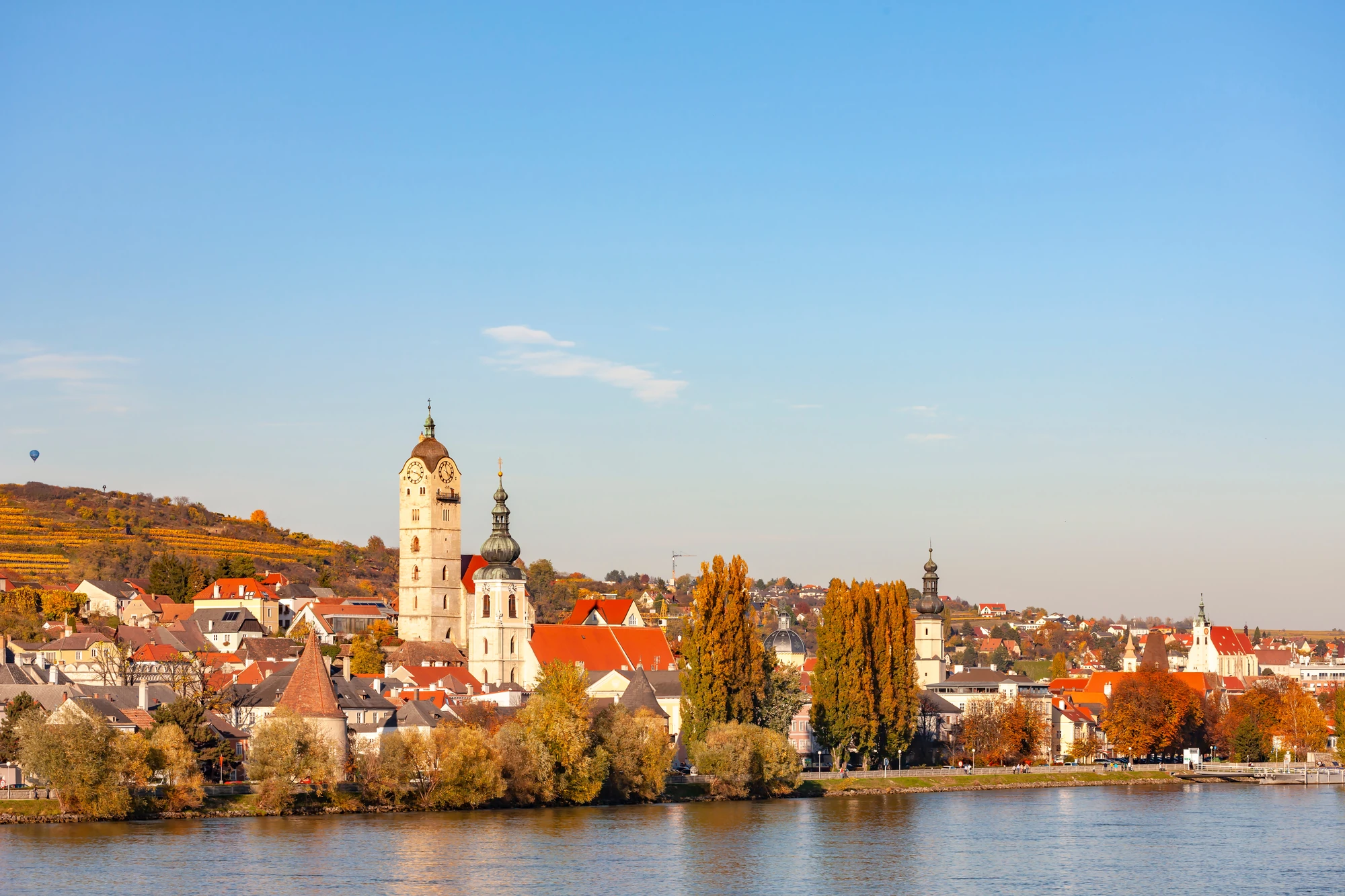 Herbstliche Stadtansicht von Krems an der Donau mit historischen Gebäuden, zwei Türmen und buntem Laub an den Bäumen.