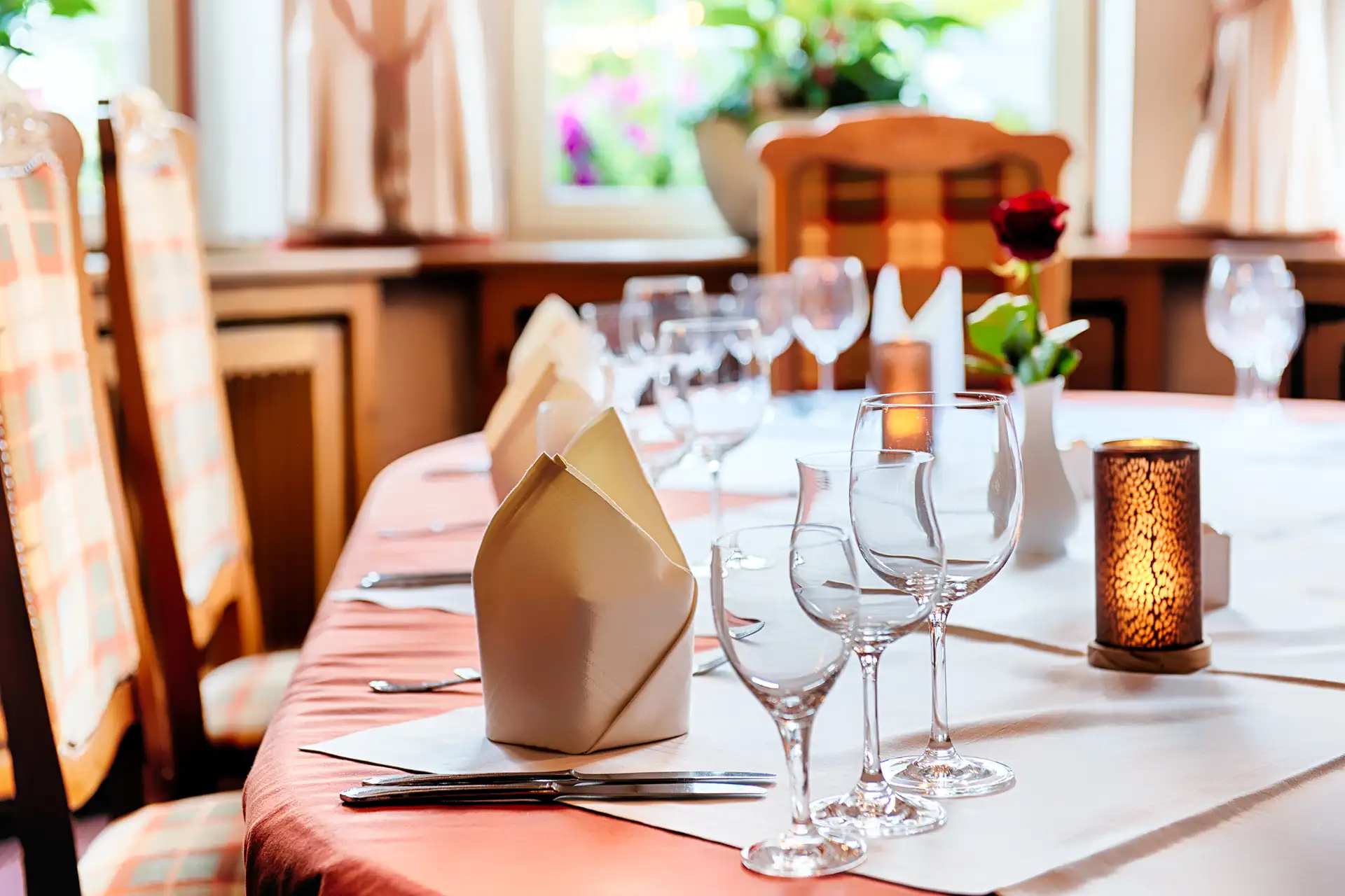 Gedeckter Esstisch im Welcome Hotel Legden mit gefalteten Servietten, mehreren Weingläsern, Besteck und einer Kerze auf einem Tischläufer