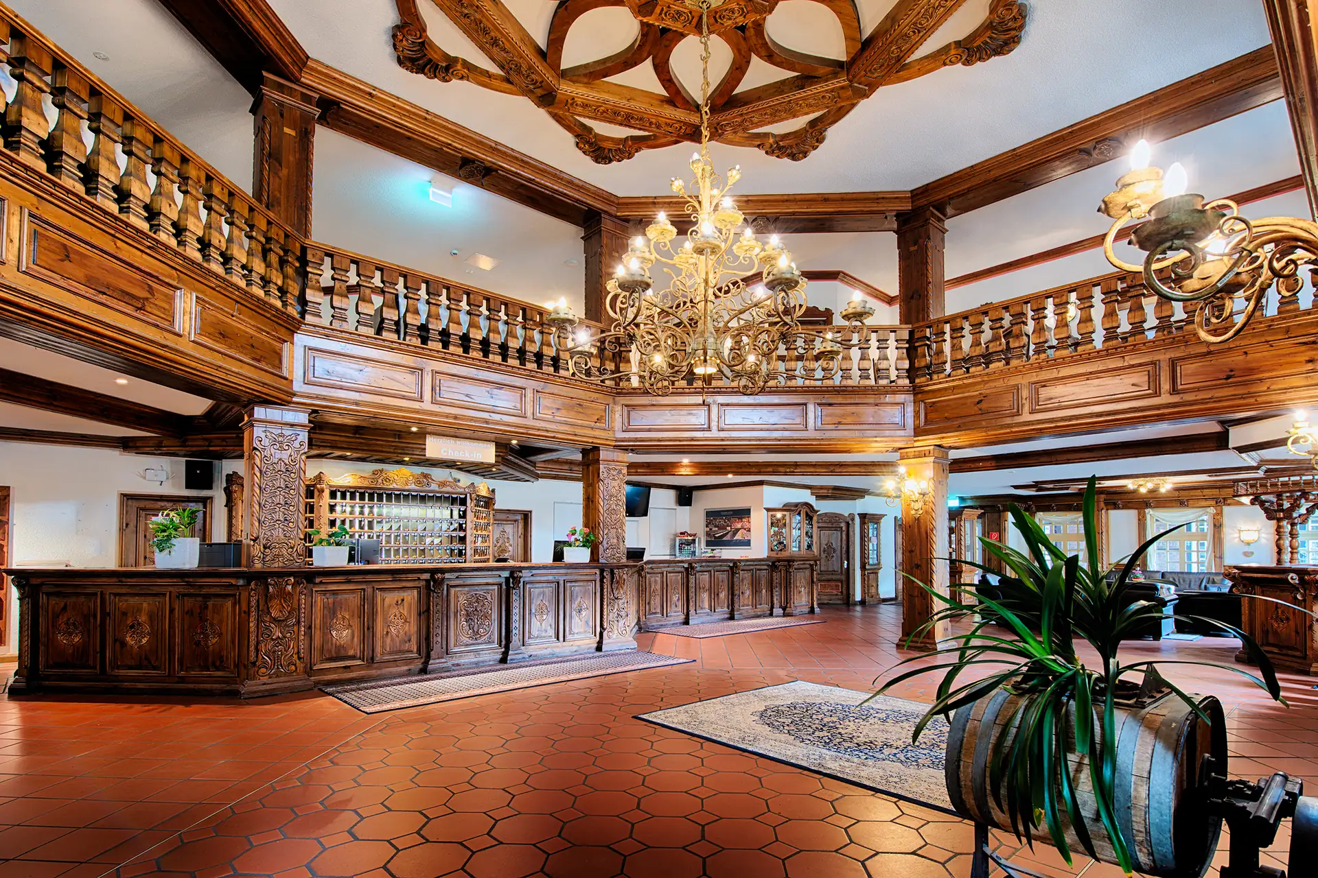 Großzügige Hotellobby mit dunklem Holzempfangstresen, Kronleuchtern und hölzernen Balkongeländern im Welcome Hotel Legden