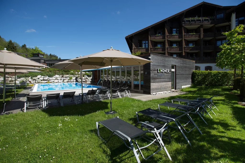 Außenansicht auf den Außenpool des Lindner Parkhotel & Spa Oberstaufen Wellnesshotel Allgäu im Sommer in herrlicher Grünanlage