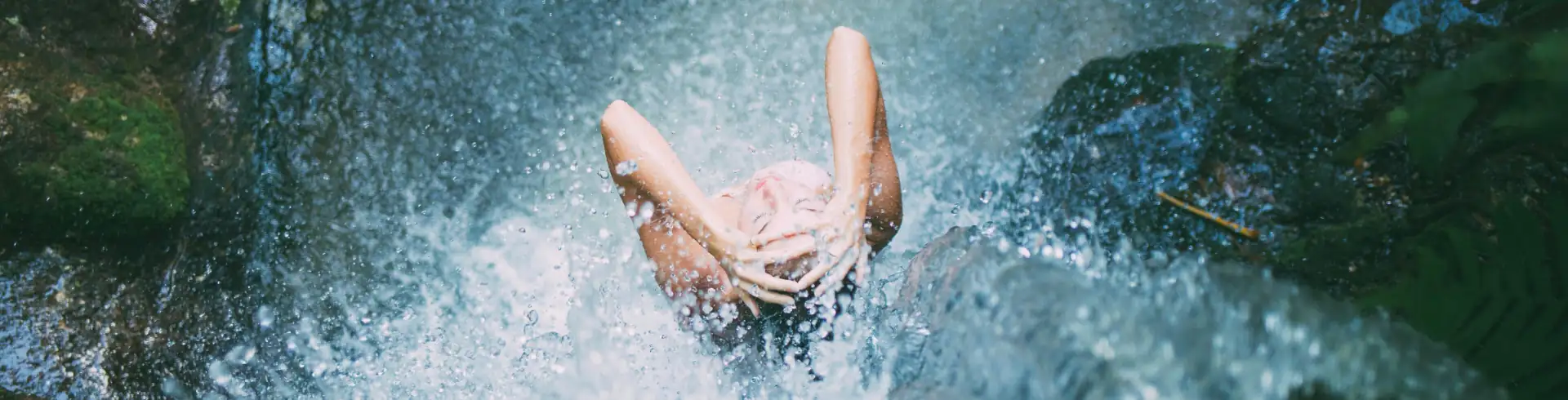 Wellnessreisen Symbolbild im Bannerformat: Blick von oben auf eine Frau, die unter einem Wasserfall steht.