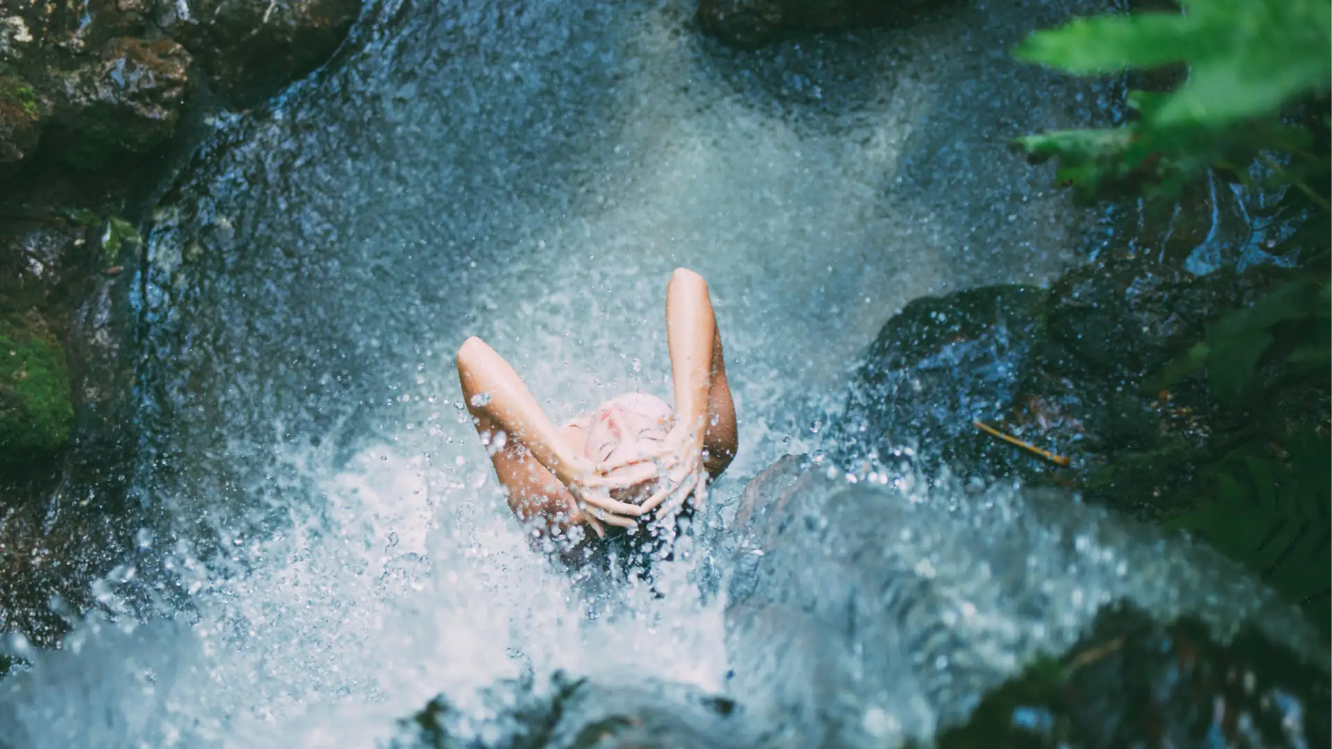 Wellnessreisen Symbolbild: Blick von oben auf eine Frau, die unter einem Wasserfall steht.