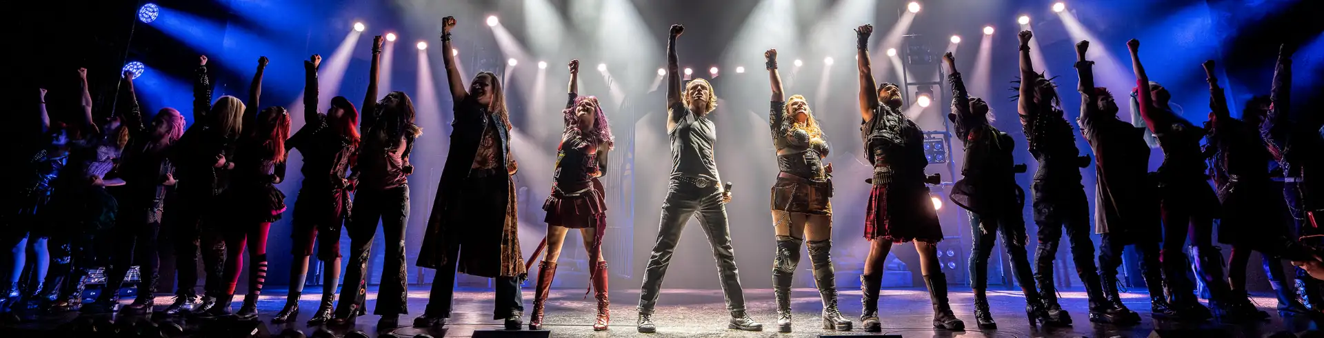 We will Rock You – Das Musical in Stuttgart Banner: Menschen auf Bühne mit erhobenen Fäusten, beleuchtet von weißen und blauen Scheinwerfern.