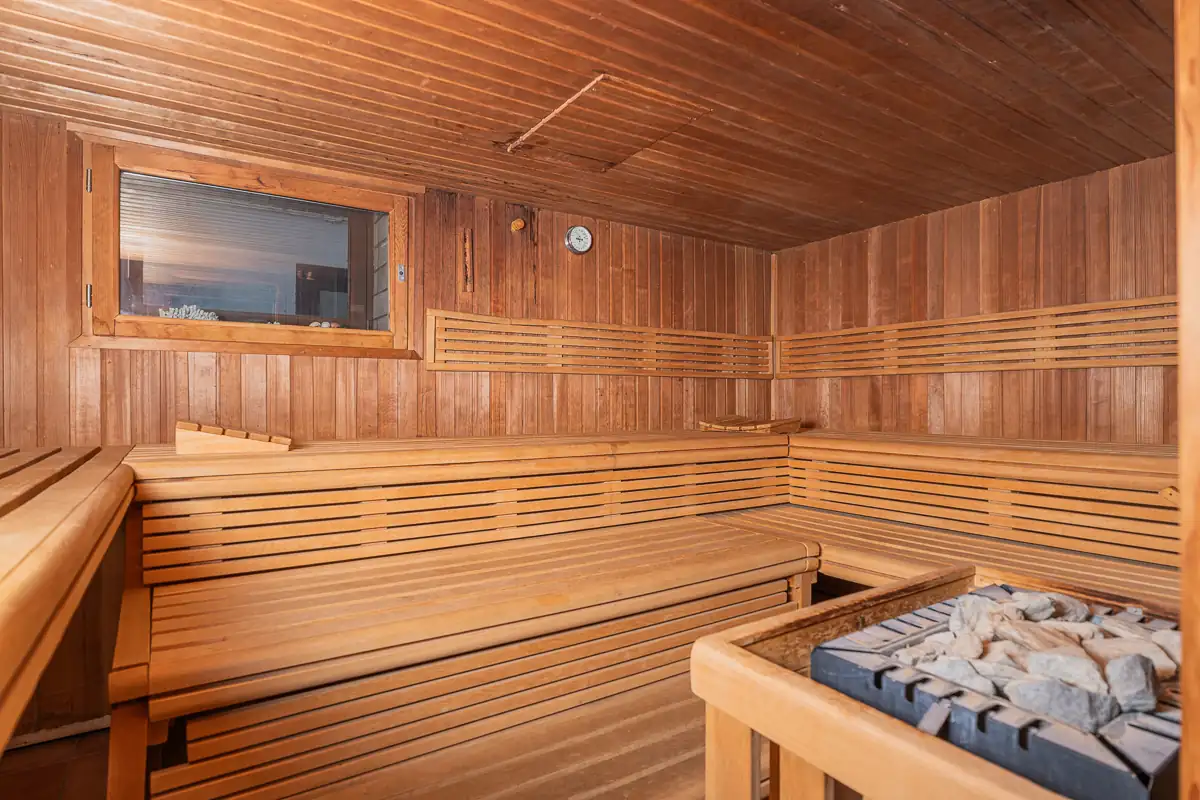 Finnische Sauna mit Holzbänken in L-Form, Holzwänden und Saunaofen mit Steinen im Hotel Zur Heidschnucke