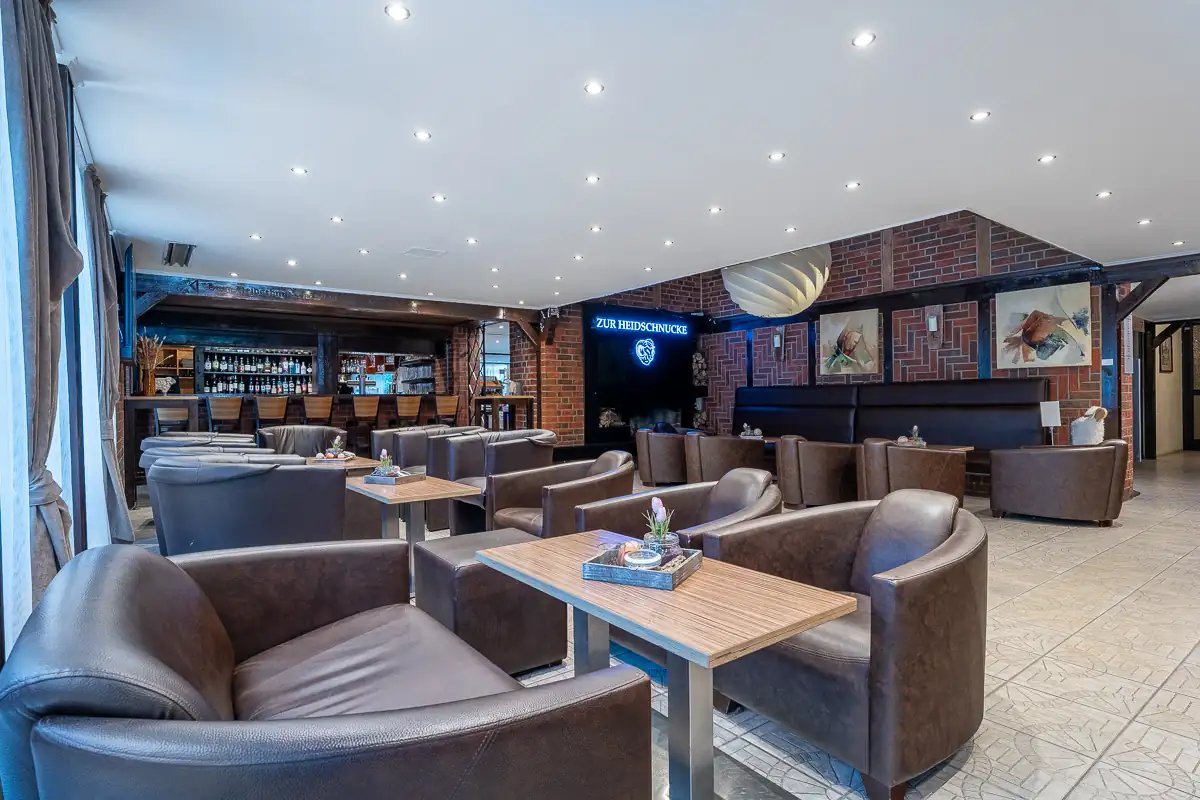 Gemütliche Lounge im Hotel Zur Heidschnucke mit braunen Ledersesseln, Holztischen, Backsteinwänden und einer beleuchteten Hoteltafel