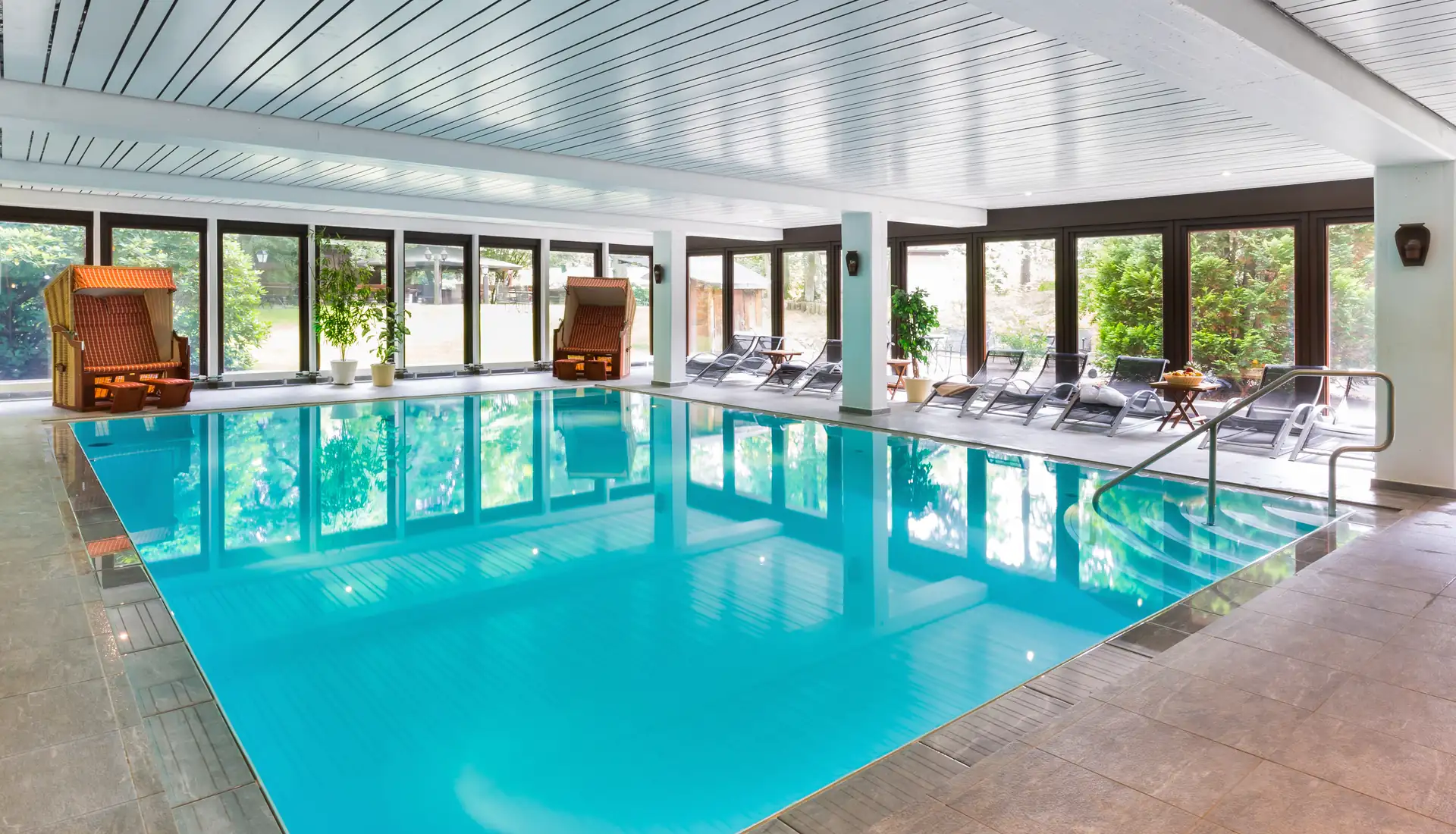 Innenansicht des Schwimmbads im Hotel Zur Heidschnucke mit rechteckigem Becken, Liegestühlen und zwei Strandkörben am Fenster