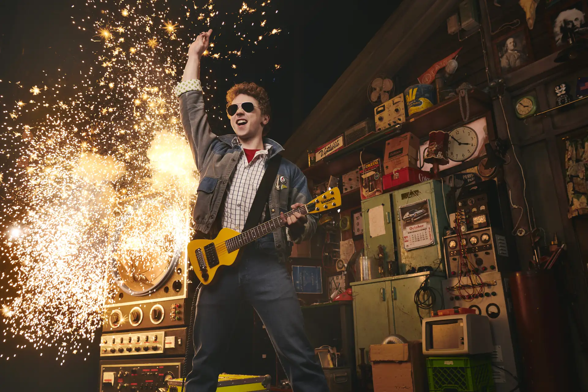 Zurück in die Zukunft – Das Musical, Szenenmotiv: Marty McFly (Caden Brauch) mit Sonnenbrille spielt E-Gitarre und hebt eine Hand, während Funken im Hintergrund sprühen.