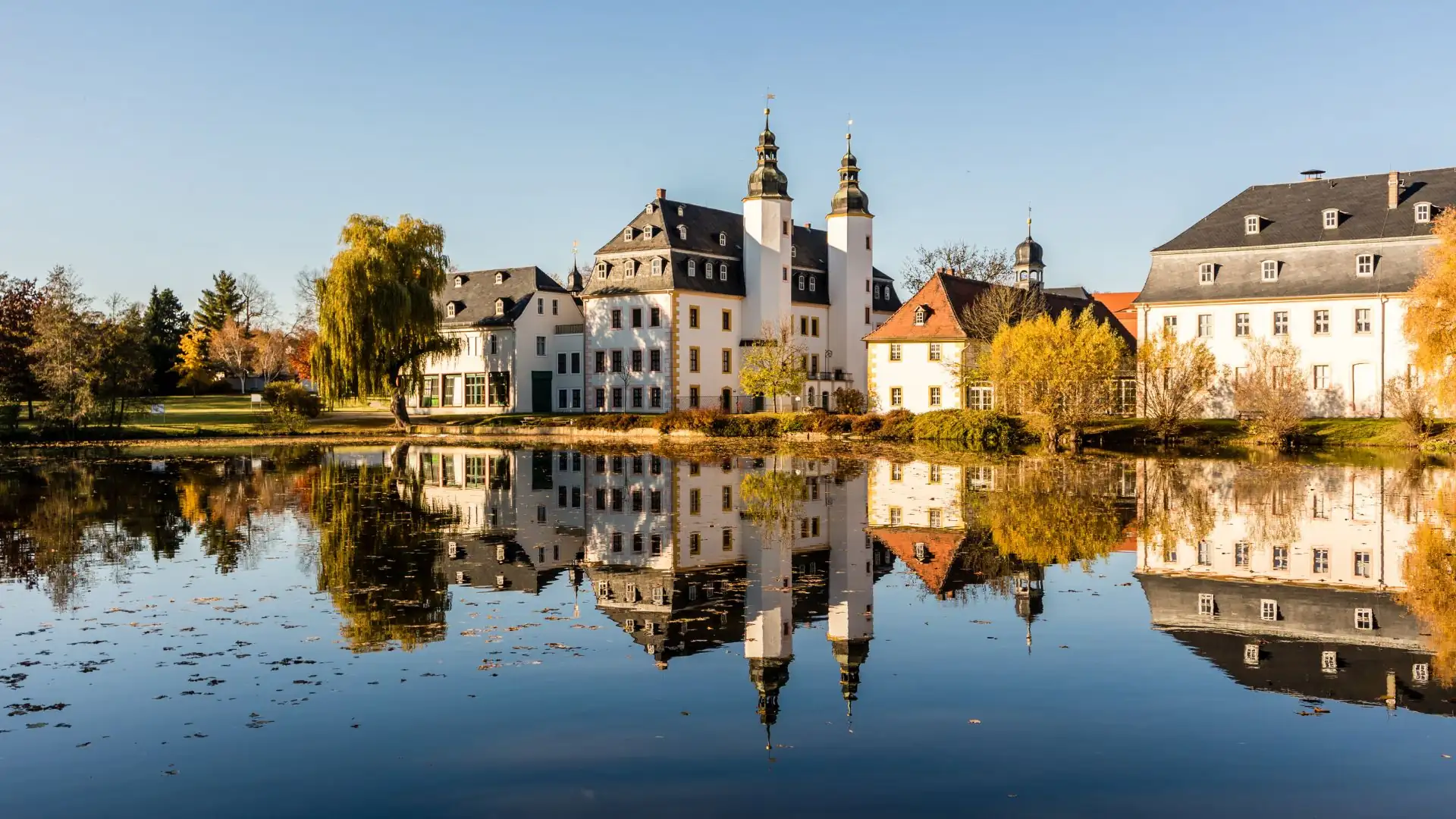 Herbstliche Landschaft mit einem historischen Schloss und ruhigem Wasser.